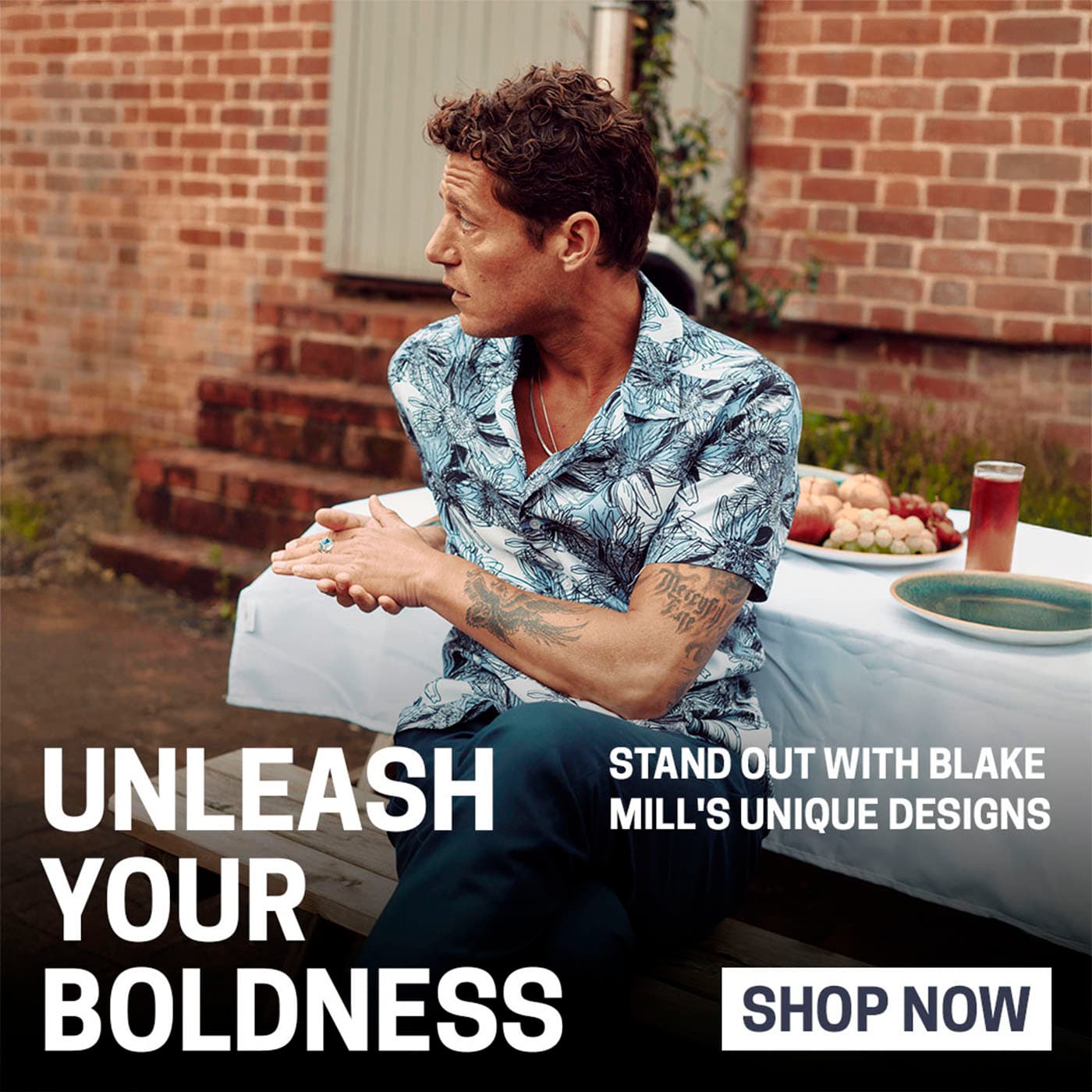 Blake Mill model in a printed short-sleeve shirt against a brick wall
